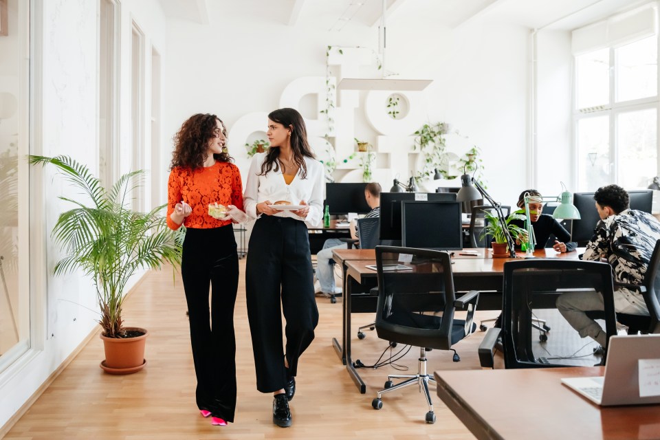 two women walking in an office with a large g on the wall