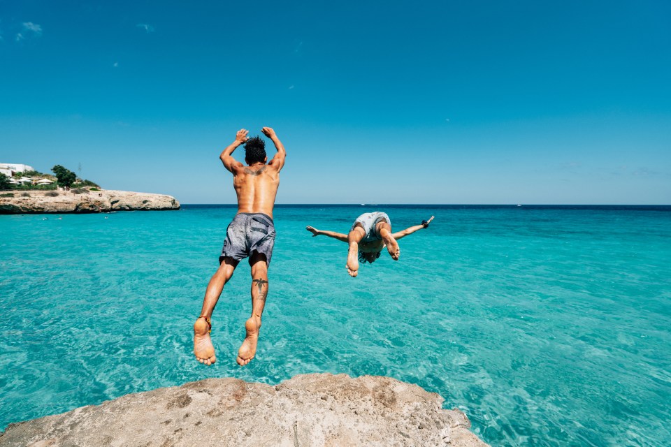 two people jumping into the ocean from a rock