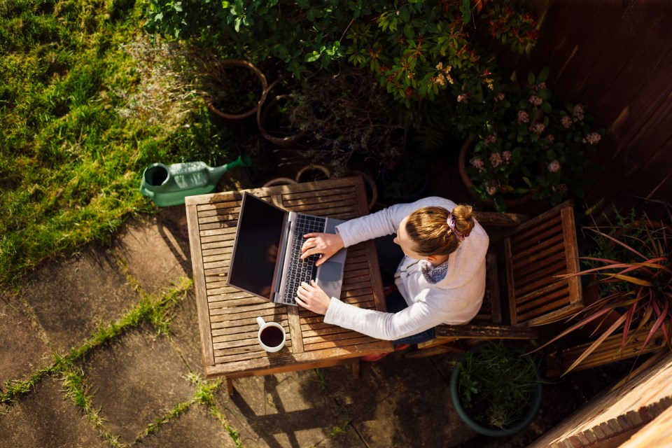 A woman working from home in her garden using a laptop