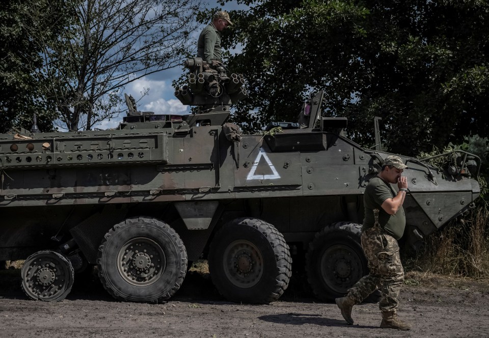 a man walks past a military vehicle with a white triangle on the side