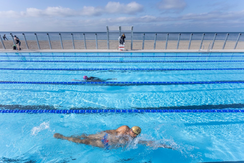 two people are swimming in a pool with a lifeguard watching