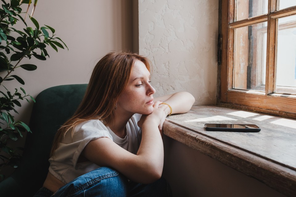 a woman sits on a window sill looking out