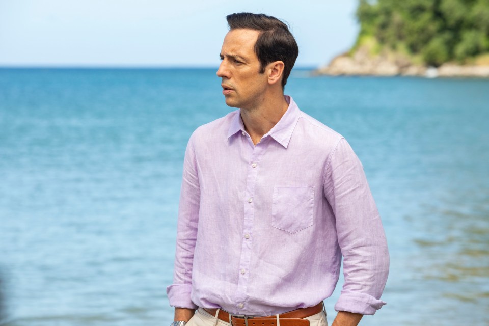 a man in a purple shirt stands in front of the ocean