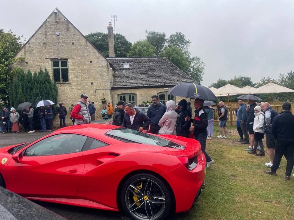 a group of people are standing around a red sports car