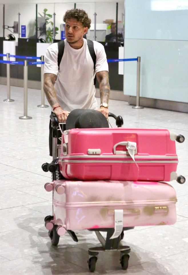 a man pushes a cart with pink suitcases on it