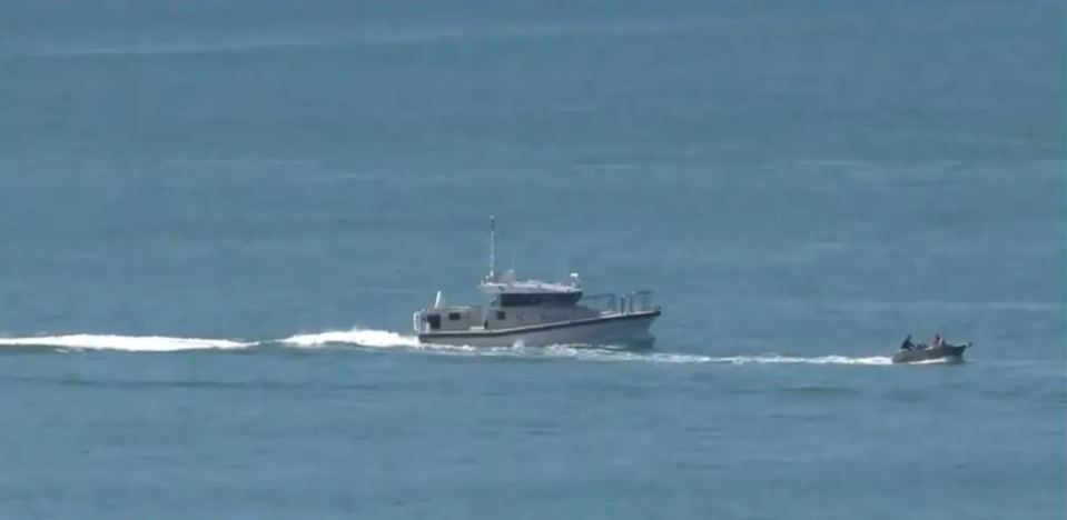 a small boat is being towed by a large boat in the ocean .