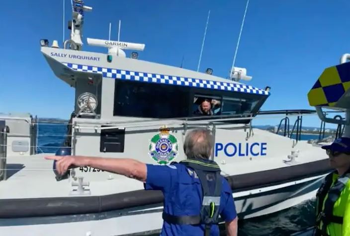 a man is pointing at a police boat in the water .