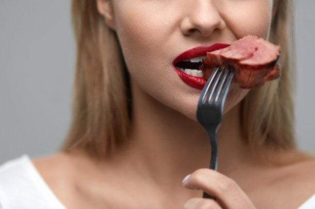 a woman with red lipstick is eating a piece of meat with a fork