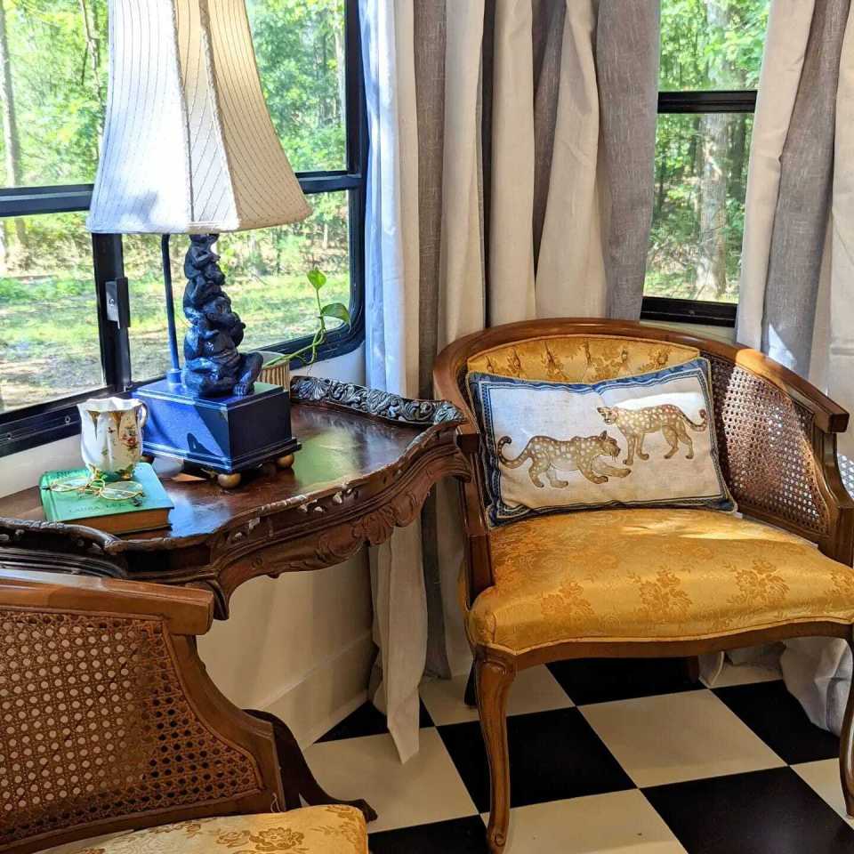 a chair with a leopard pillow sits next to a table with a lamp