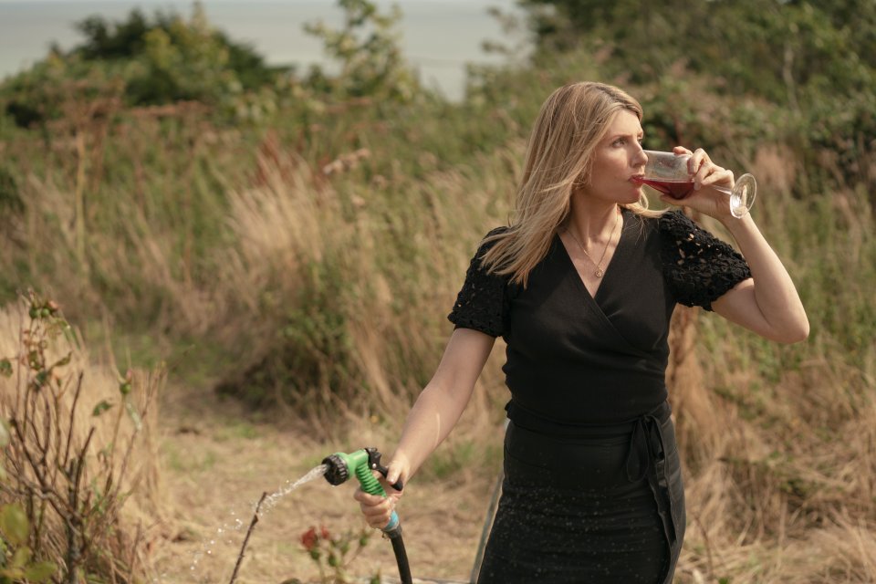 a woman in a black dress is drinking wine from a hose