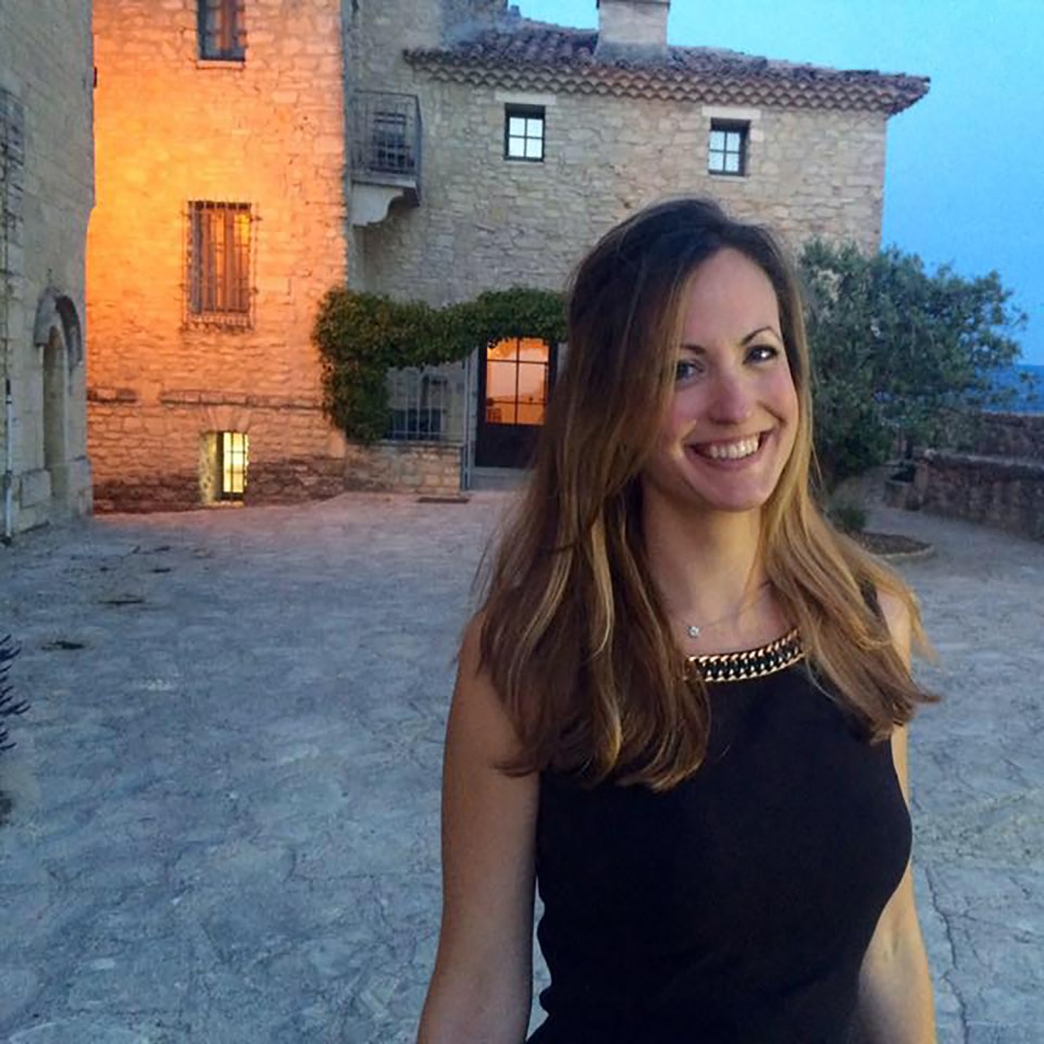 a woman in a black dress smiles in front of a stone building