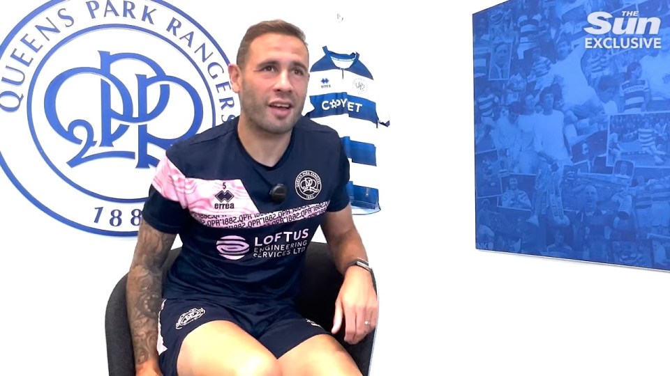 a man sitting in front of a queens park rangers logo