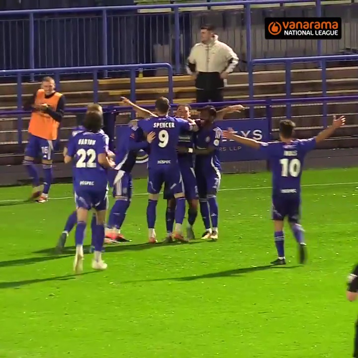 a group of soccer players are celebrating a goal in front of a vanarama national league banner