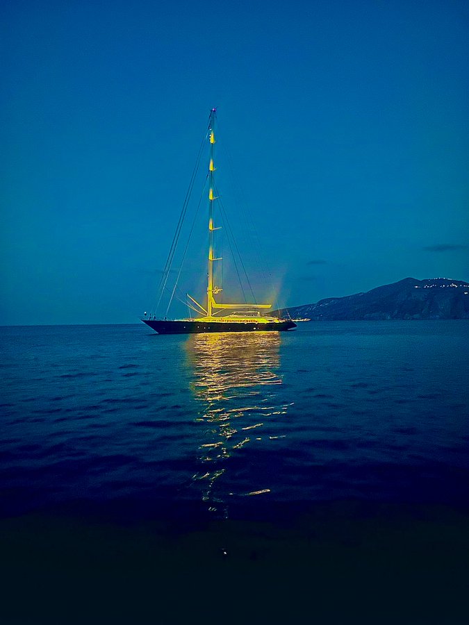 a sailboat is lit up in the middle of the ocean