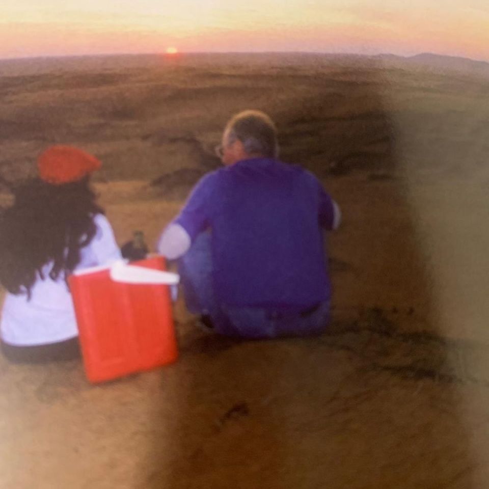 a man and a woman are sitting in the sand watching the sun set