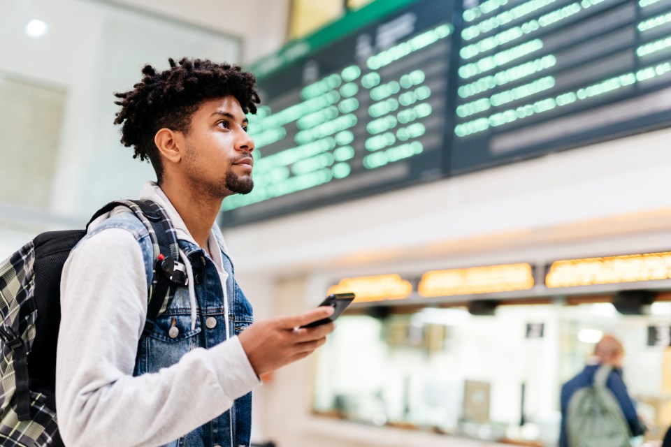 a man looking at his phone in front of a departure board