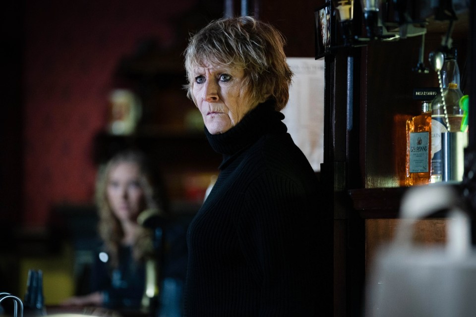 a woman in a black turtleneck stands in front of a bottle of gin