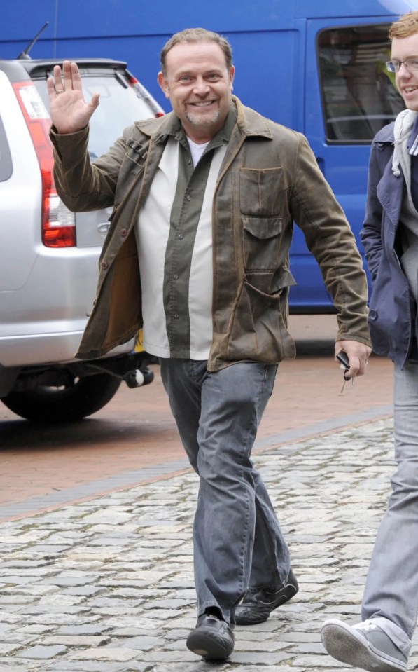 a man in a brown jacket is walking down a cobblestone street