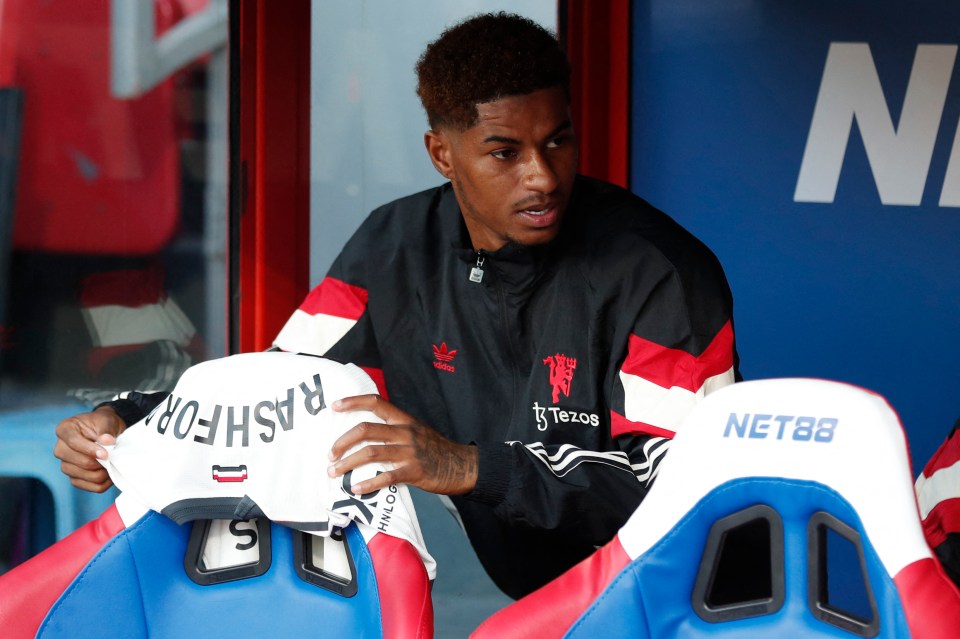 a man holds up a jersey with the name rashford on it