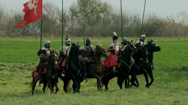 a group of men riding horses in a field with a red flag in the background