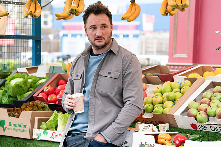 a man stands in front of boxes of fruit and vegetables including one that says romador