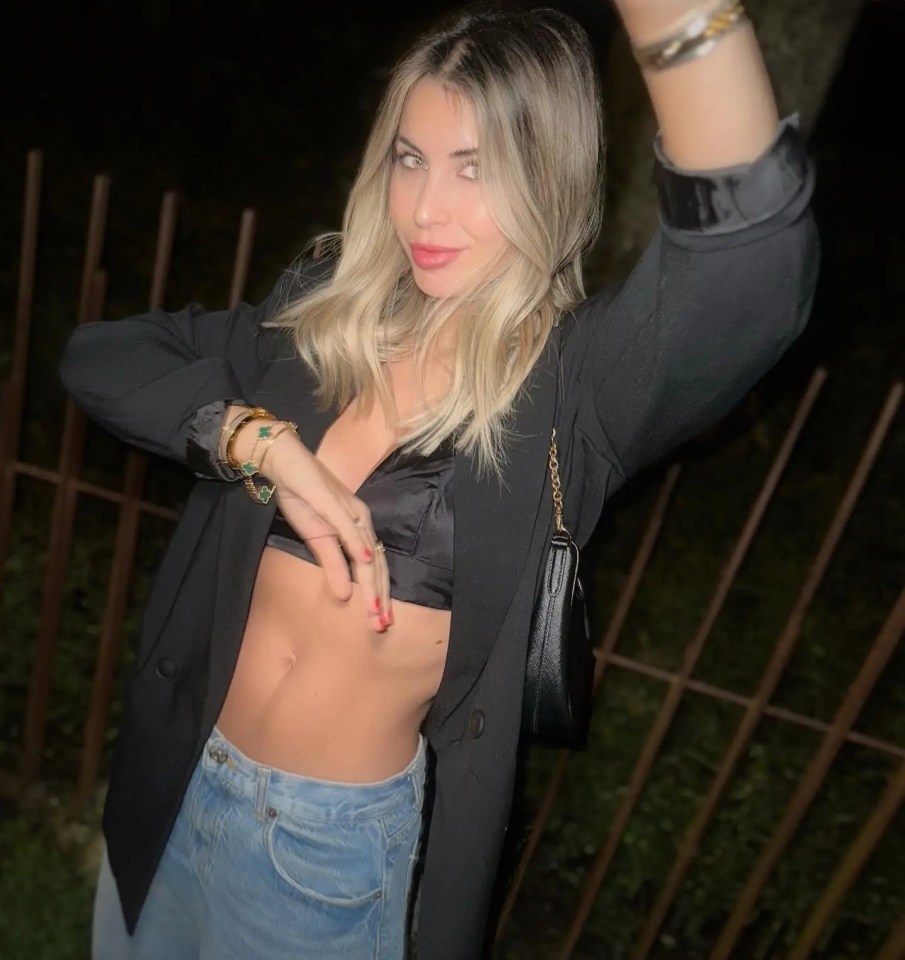 a woman wearing a black blazer and a crop top stands in front of a fence