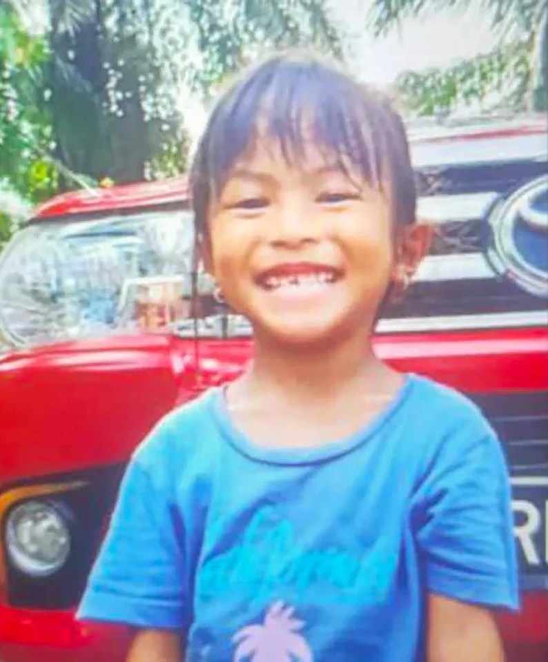 a young boy is smiling in front of a red car .