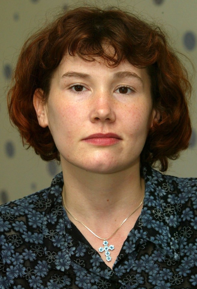 a woman with red hair is wearing a blue cross necklace