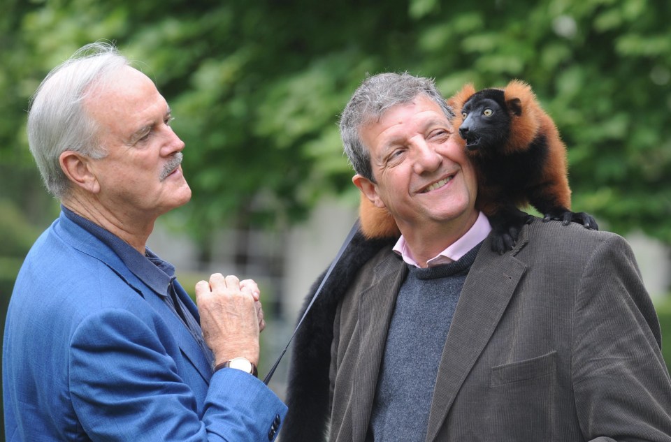 John Cleese watches as Chris Serle meets Colin the red ruffed lemur during a visit to Bristol Zoo Gardens