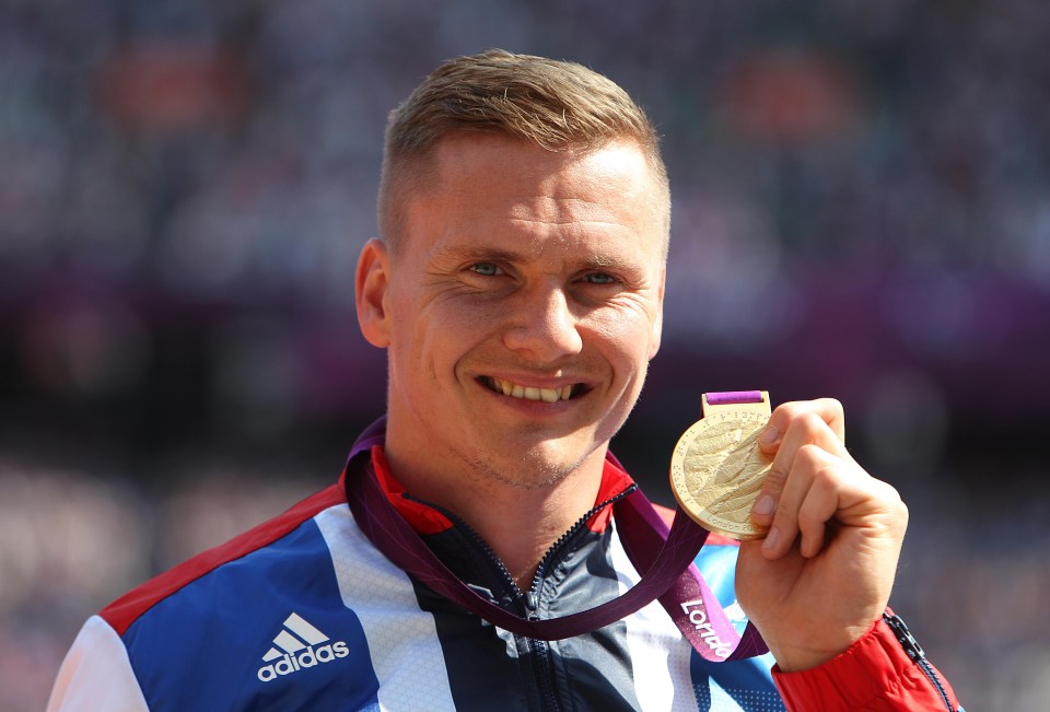 a man wearing an adidas jacket holds up a gold medal