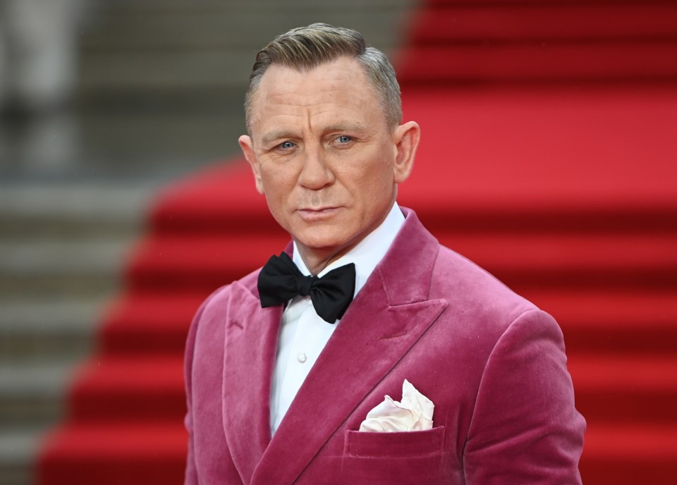 a man in a pink suit and bow tie stands on a red carpet