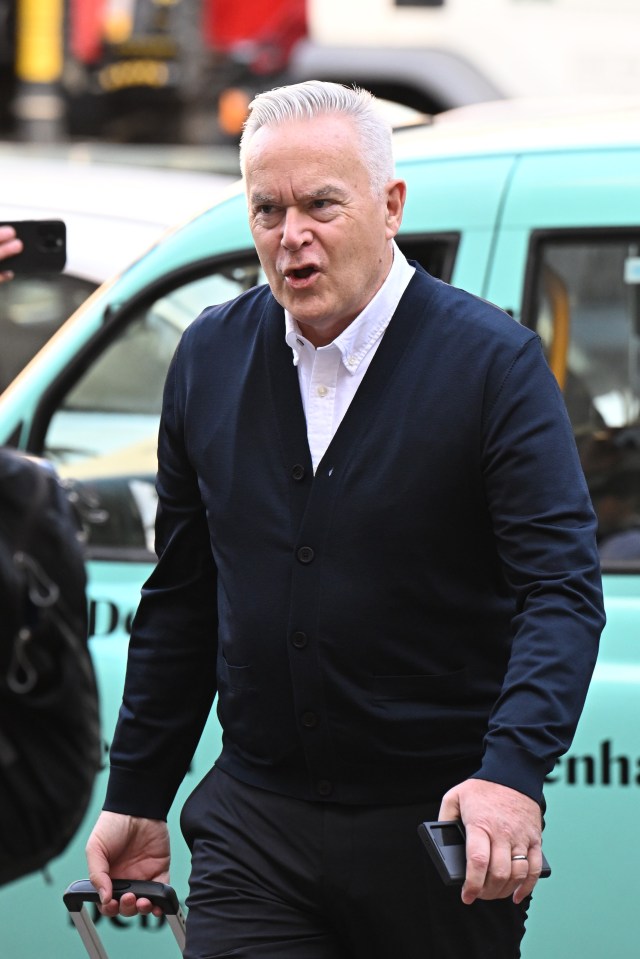 a man in a blue cardigan is standing in front of a car that says do not enter