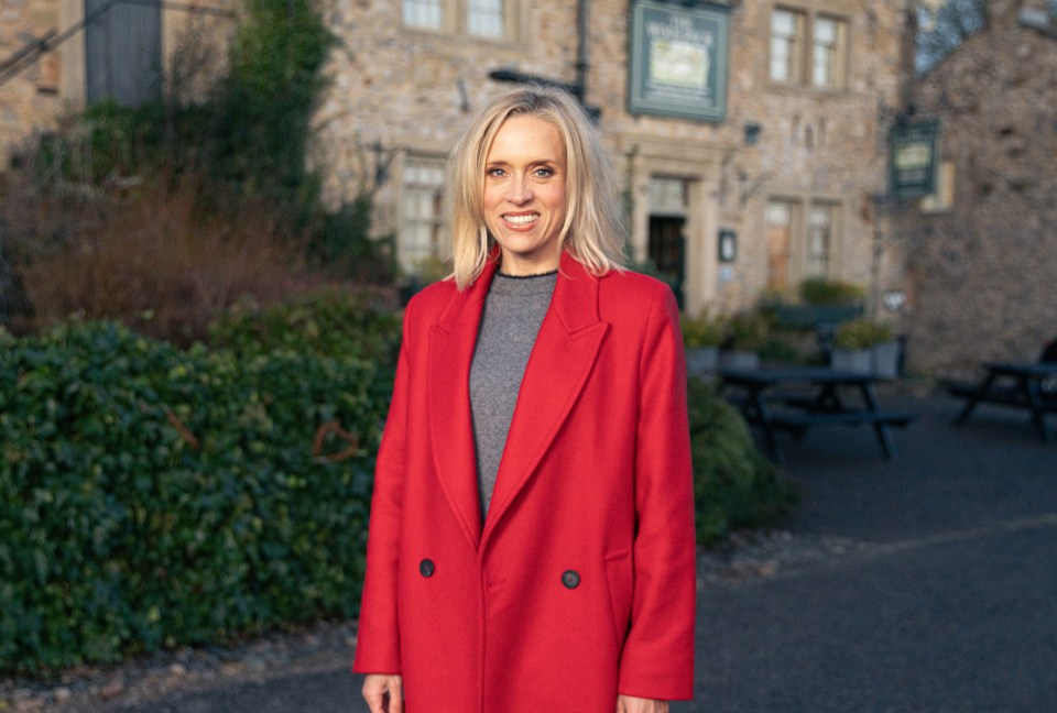 a woman in a red coat stands in front of a stone building