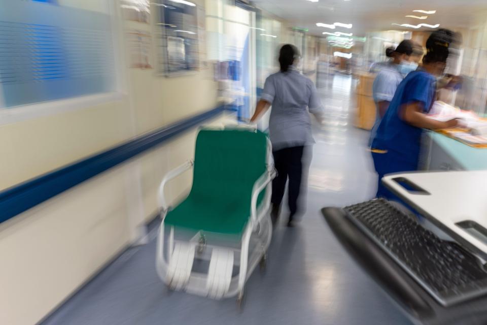 a blurred image of a hospital hallway with a nurse pushing a green chair