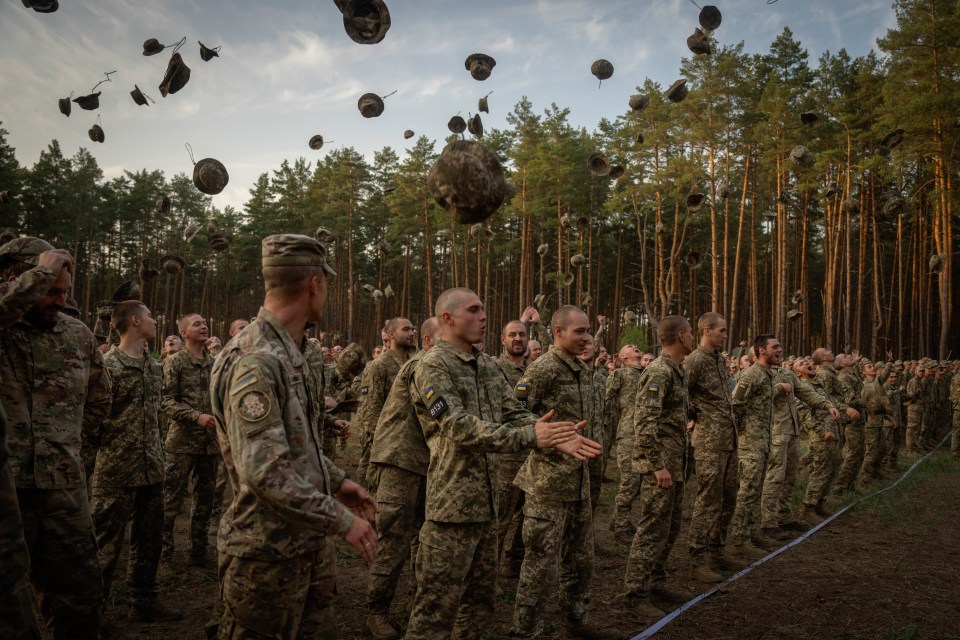 a group of soldiers are standing in a line with their hats being thrown in the air