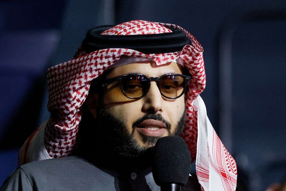 a man wearing sunglasses and a keffiyeh is speaking into a microphone