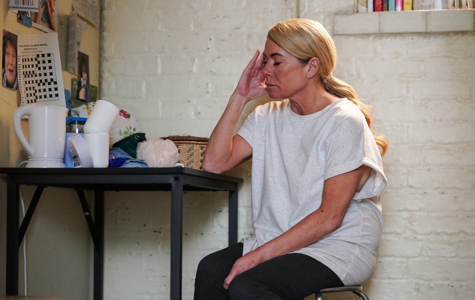 a woman sits at a table with a crossword puzzle on the wall behind her