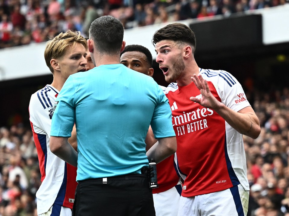 soccer player wearing a red emirates fly better jersey talking to a referee