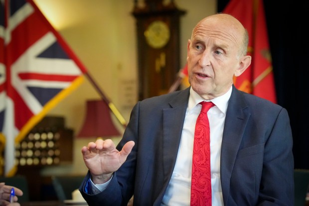 a man in a suit and red tie is talking in front of a flag