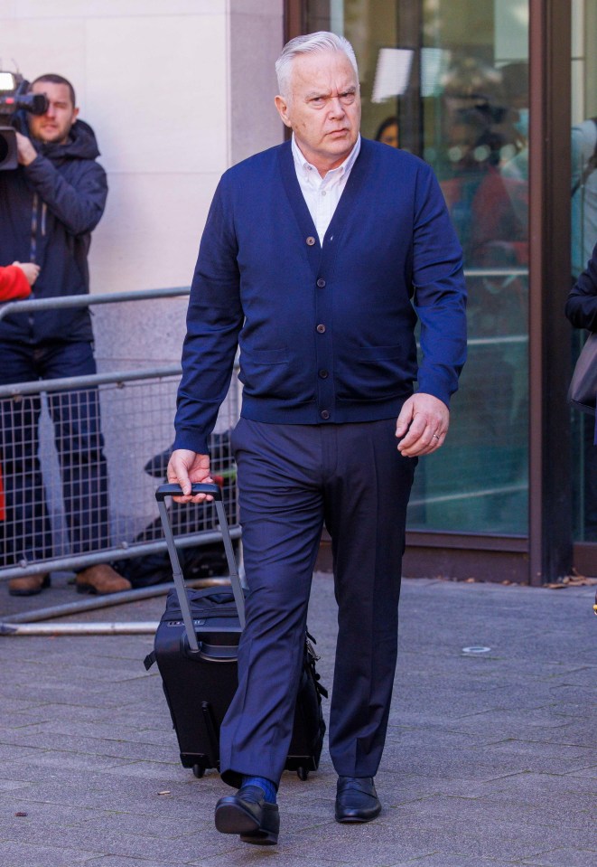 a man in a blue cardigan is pulling a suitcase