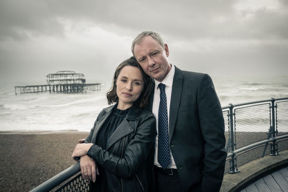 a man in a suit and tie stands next to a woman in a leather jacket