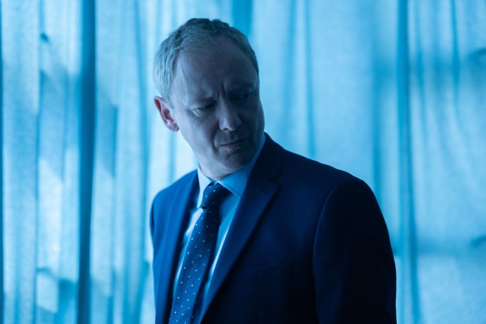 a man in a suit and tie stands in front of a blue curtain