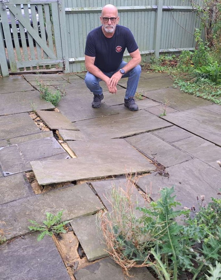 a man squatting on a patio with a fence in the background