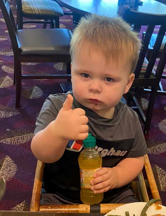 a young boy giving a thumbs up while holding a bottle of orange juice