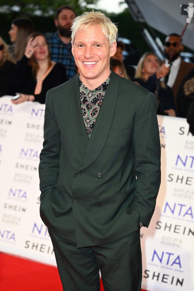 a man in a green suit smiles on the red carpet