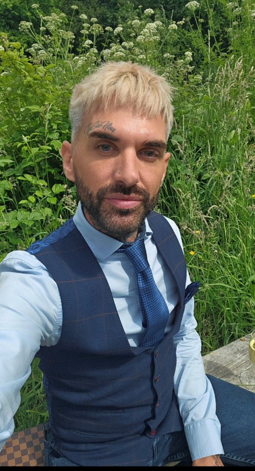 a man with a tattoo on his face is wearing a blue vest and tie