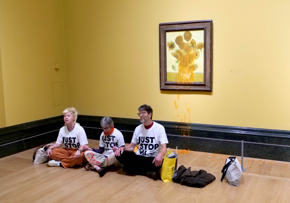 three people wearing just stop shirts sit on the floor in front of a painting