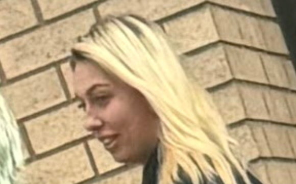 a woman with blonde hair is standing in front of a brick wall .