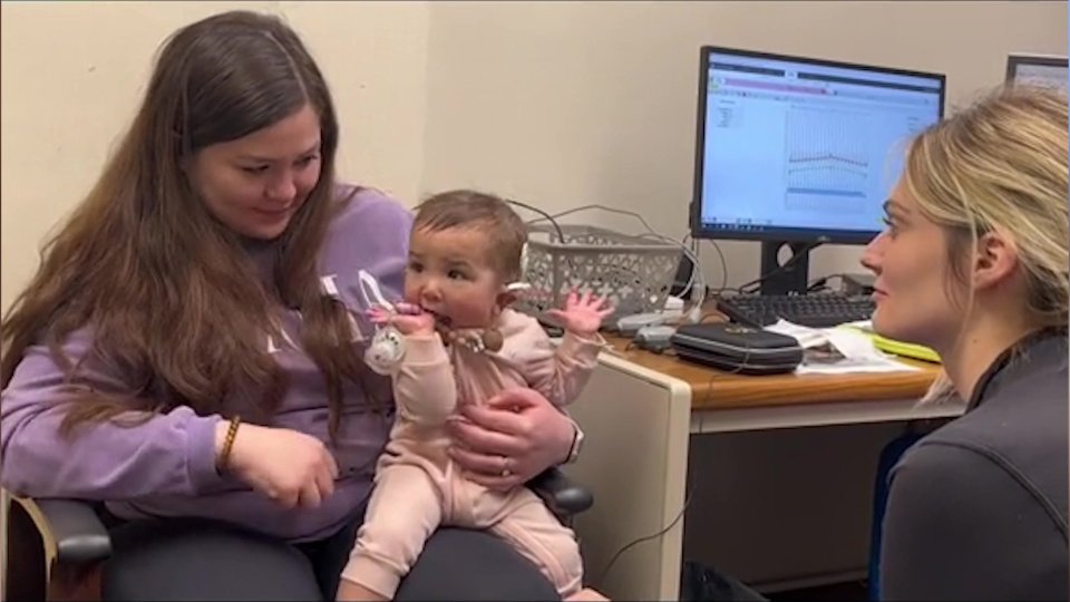 a woman holding a baby in front of a computer monitor