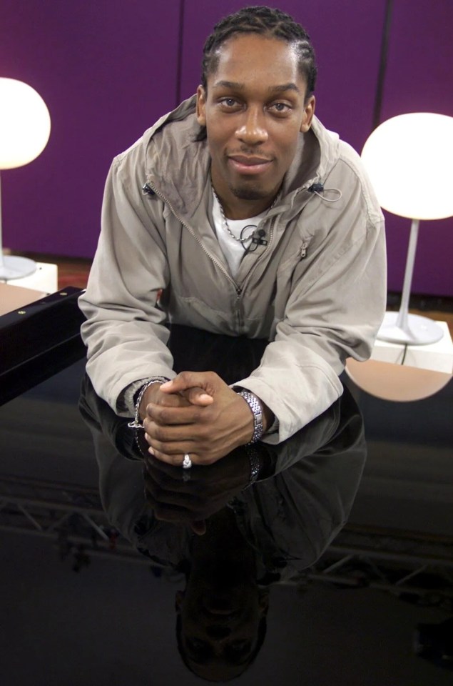 a man in a jacket sits at a table with his hands folded